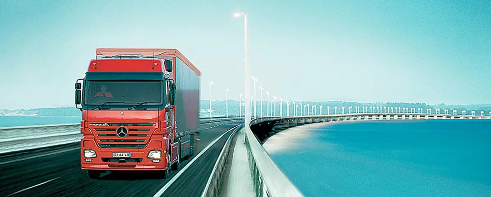 Red haulage truck carrying freight along a coastal highway bridge